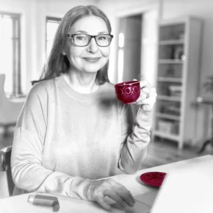 Eine Frau mittleren Alters sitz am Tisch und trinkt eine Tasse Kaffee.