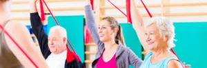 Zwei Frauen und ein Mann machen Gymnastik mit einem Terraband und sind dabei fröhlich