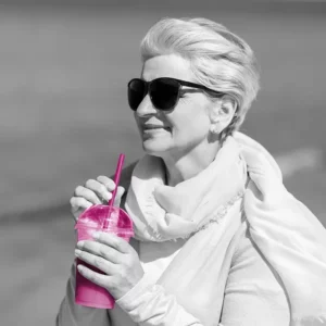 Frau mit Sonnenbrille und einem pinken Becher in der Hand